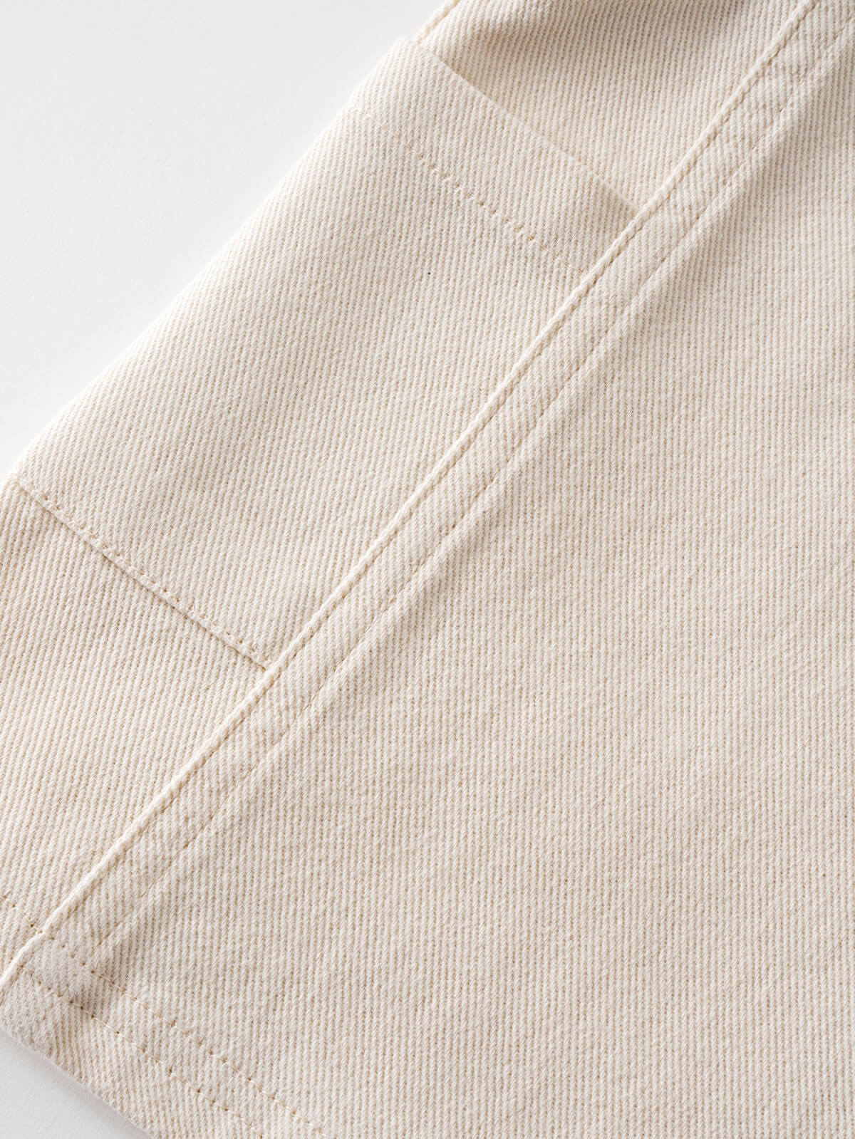 Close-up of cream-colored fabric with stitched seams and textured weave Twill Pinafore Dress - Salt Girls