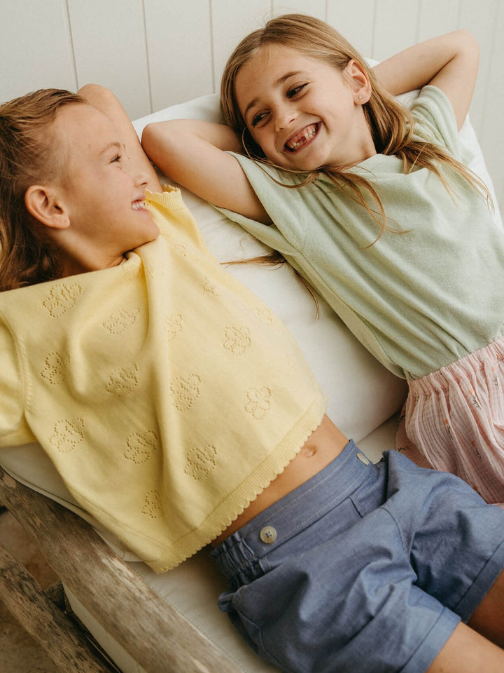 Two children lying on a couch with a yellow blanket, smiling.