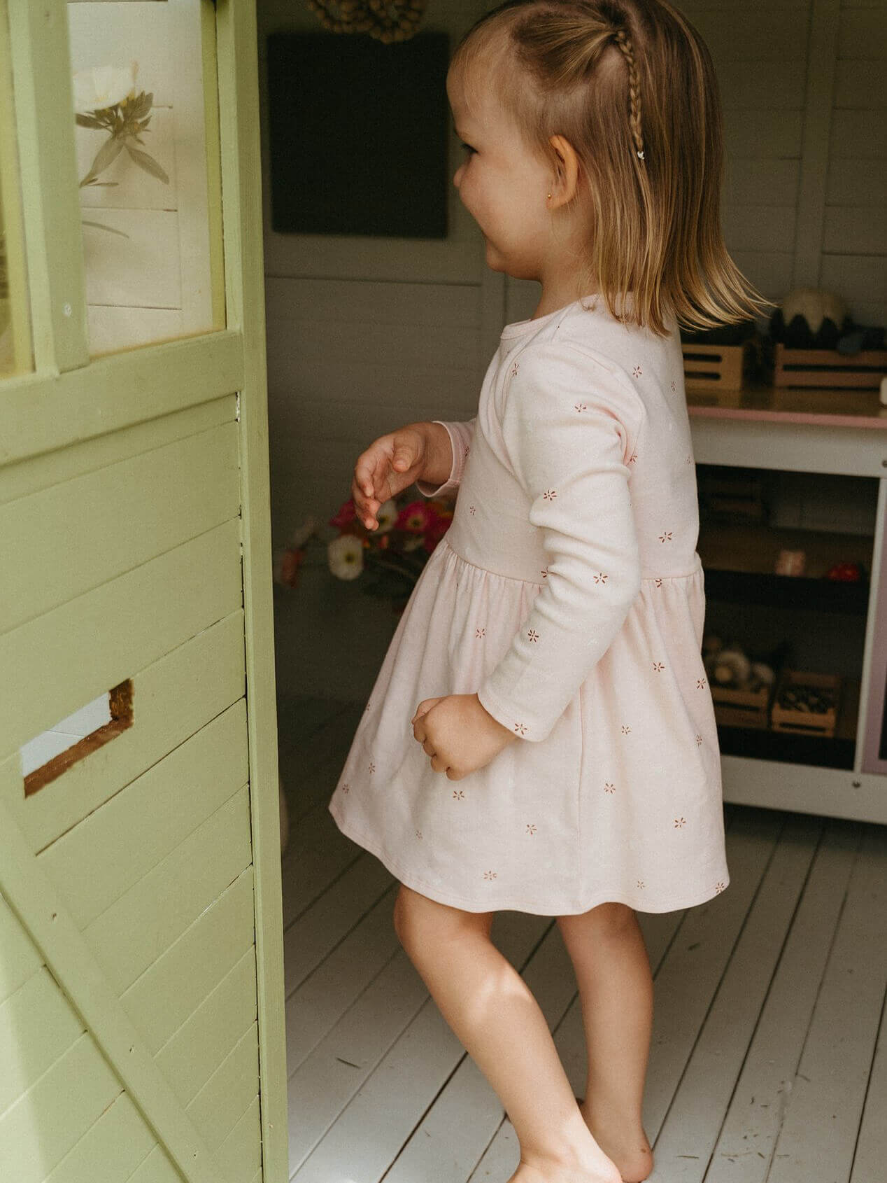 Young girl in a light dress standing inside a playhouse.