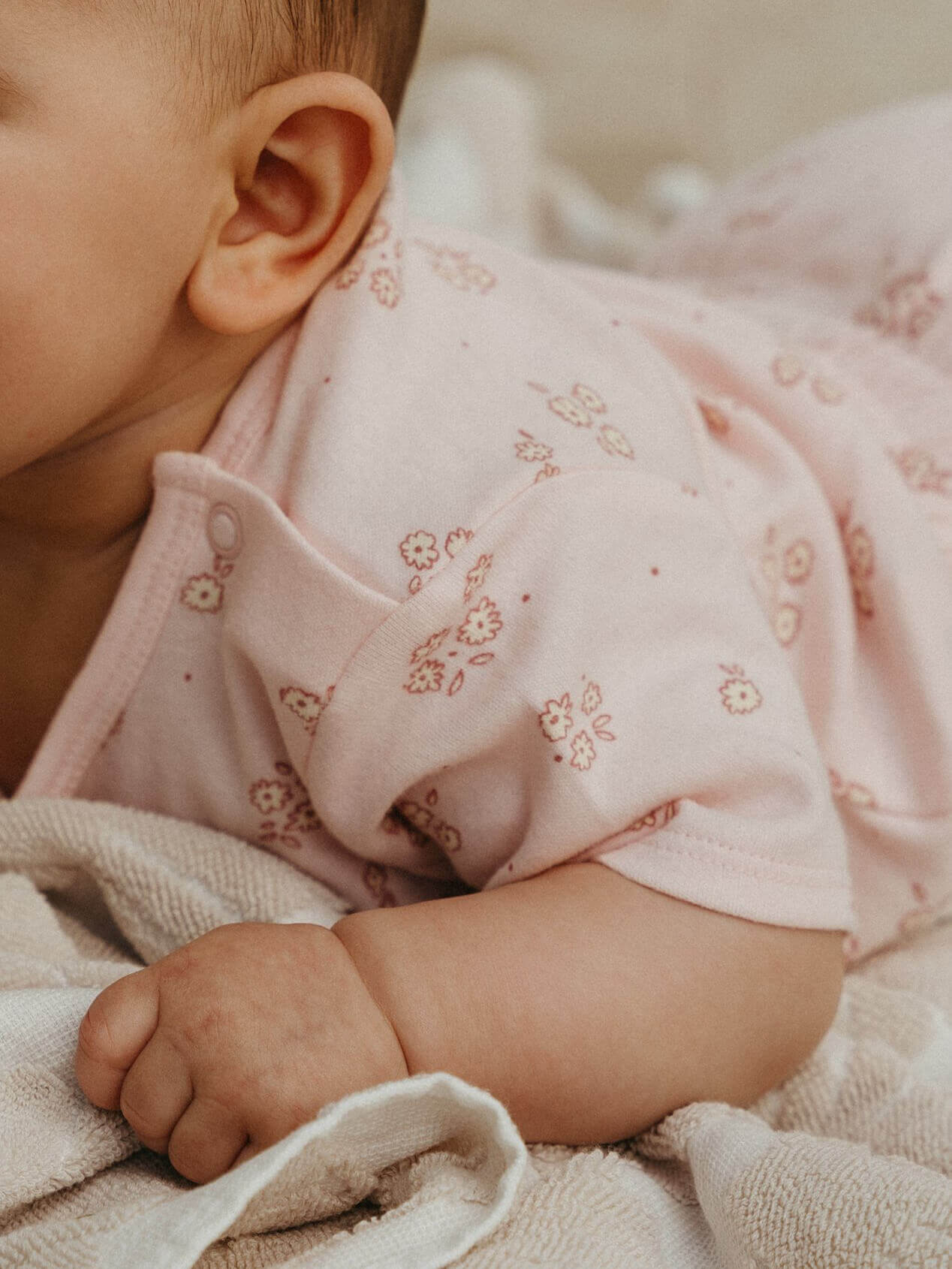 Close-up of a baby in a pink outfit with floral patterns, lying on a soft surface.