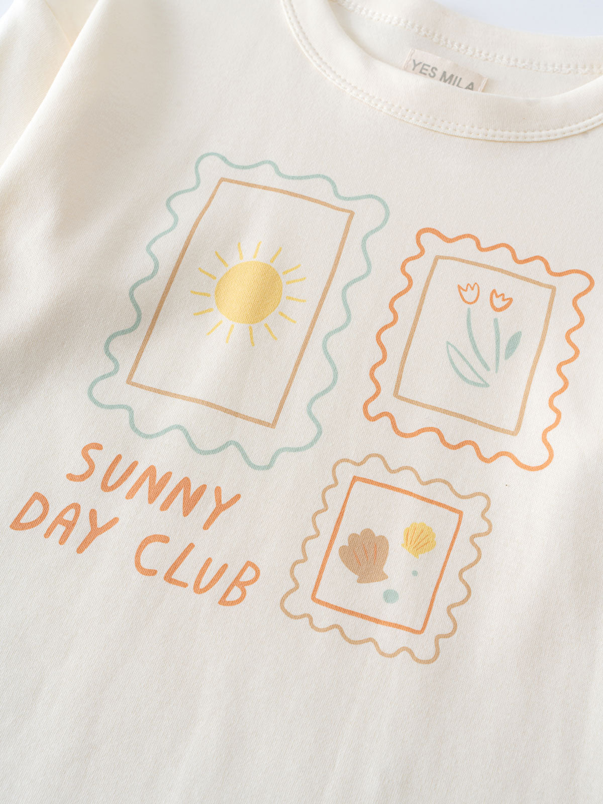 Close-up of a cream-colored shirt with three postage stamp graphics and text Zoey Long Sleeve Tee - Sunny Club Day Girls
